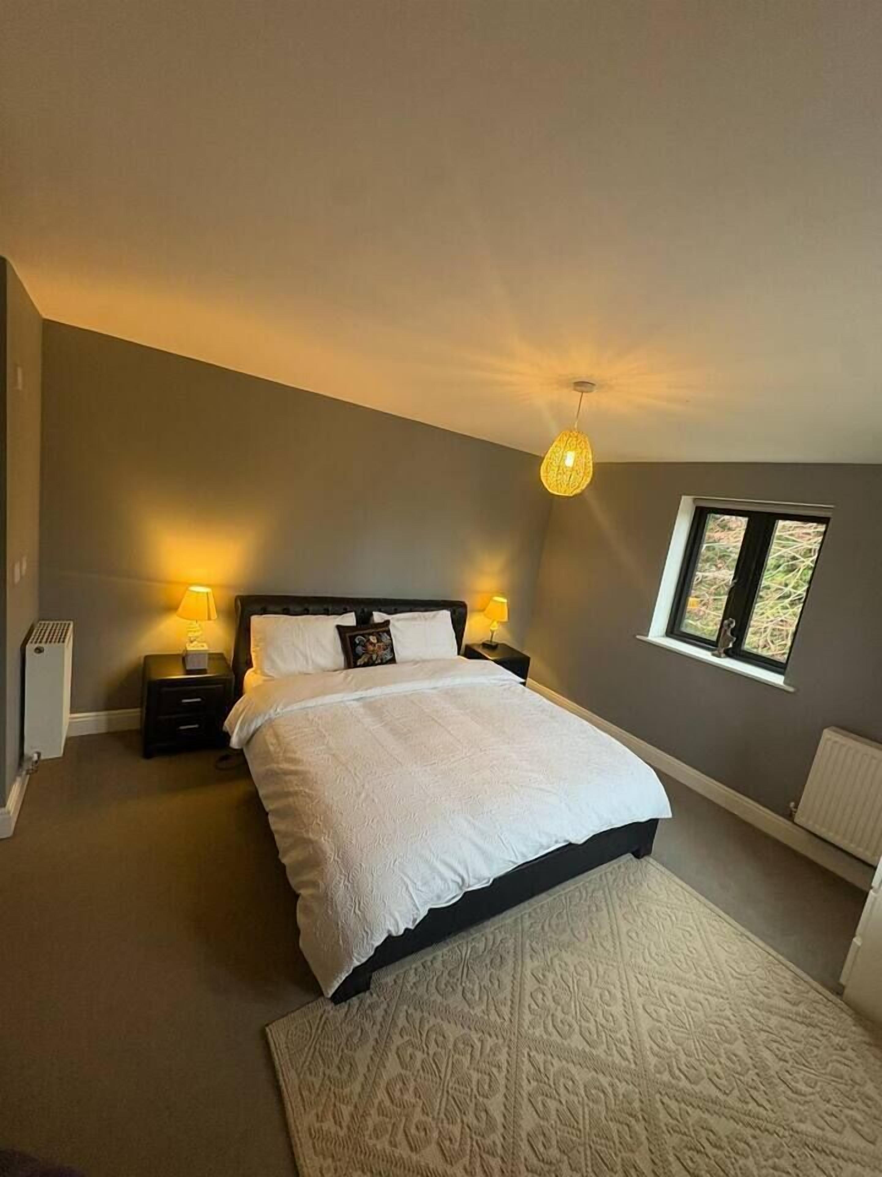 A bedroom with a bed, nightstands, a lamp, a window, and a radiator.