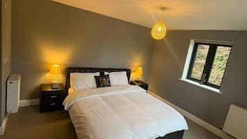 A bedroom with a bed, nightstands, a lamp, a window, and a radiator.