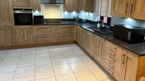 A modern kitchen with wooden cabinets, a stainless steel range hood, and a black microwave. - #100 Comfortable 4-Bed House in Rugby (Warwickshire)
