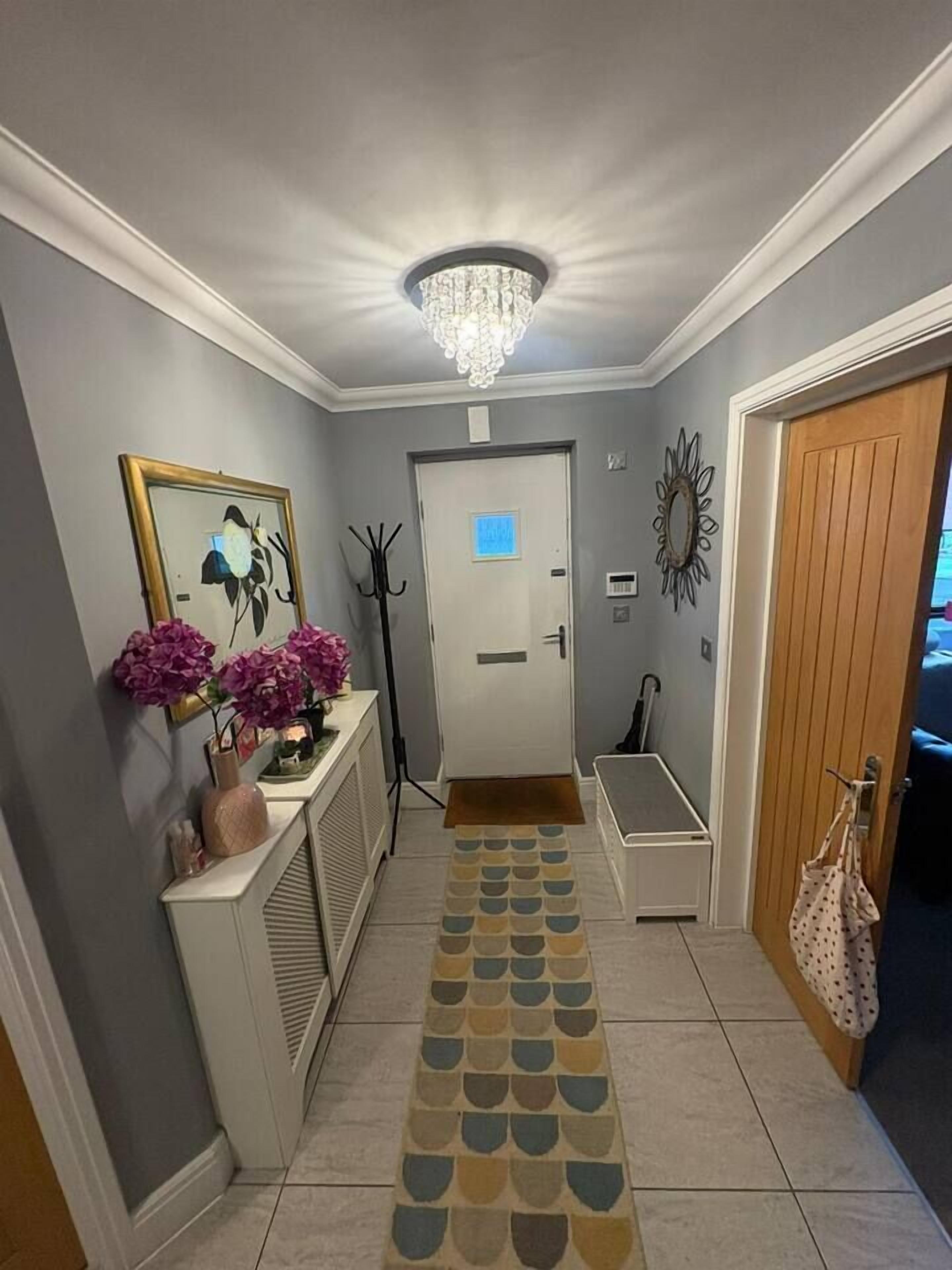 A hallway with a patterned rug, a coat rack, a bench, and a door with a light switch.