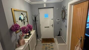 A hallway with a patterned rug, a coat rack, a bench, and a door with a light switch.