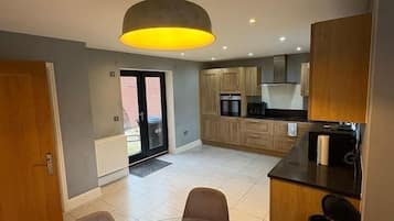 A modern kitchen with wooden cabinets, a dining area with a table and chairs, and a hanging light fixture.