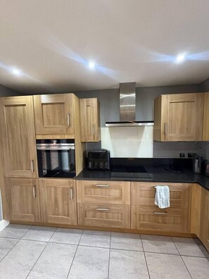 A kitchen with wooden cabinets, a black countertop, and a stainless steel range hood. - #100 Comfortable 4-Bed House in Rugby (Warwickshire)