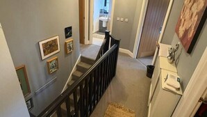 A hallway with a staircase, a radiator, and framed pictures on the wall. - #100 Comfortable 4-Bed House in Rugby (Warwickshire)