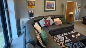 A modern living room with a sectional sofa, a coffee table, and a chandelier. - #100 Comfortable 4-Bed House in Rugby (Warwickshire)