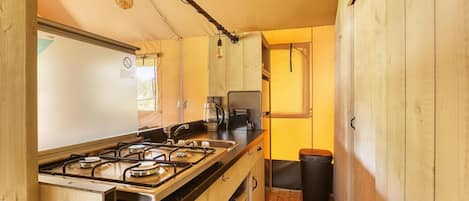 A compact kitchen with a gas stove, coffee maker, and a trash bin.