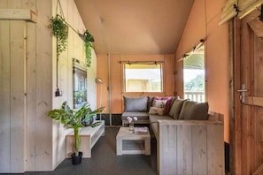A cozy room with a wooden bench, a sofa, and a small table. There are plants and a window with a view.