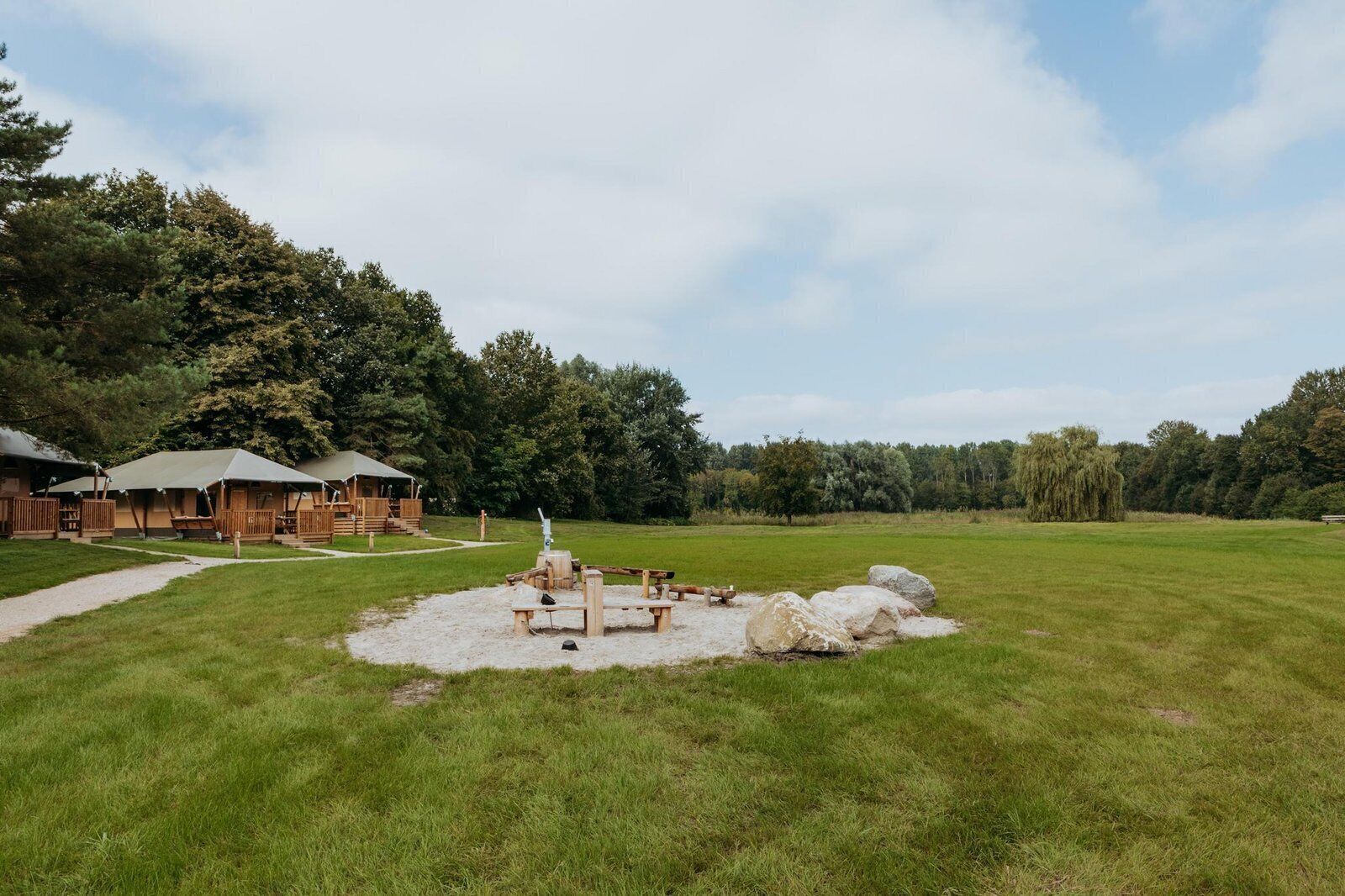 Un terrain de camping doté de cabanes en bois, d’un espace pique-nique et d’un grand champ herbeux.
