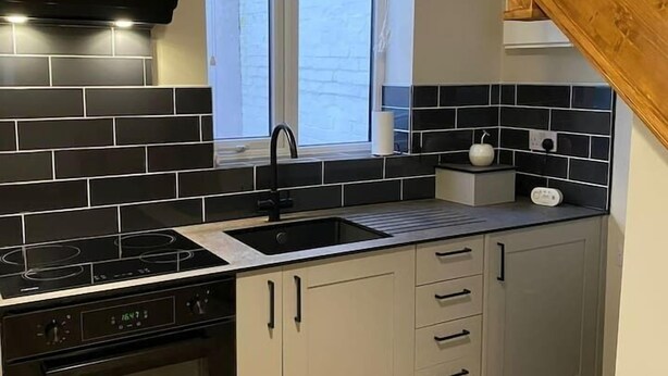 Une cuisine avec des carreaux noirs et blancs, un four encastré, une cuisinière et une fenêtre avec des stores.