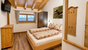 Une chambre à coucher avec un lit en bois, une armoire, un téléviseur et une fenêtre avec des rideaux.