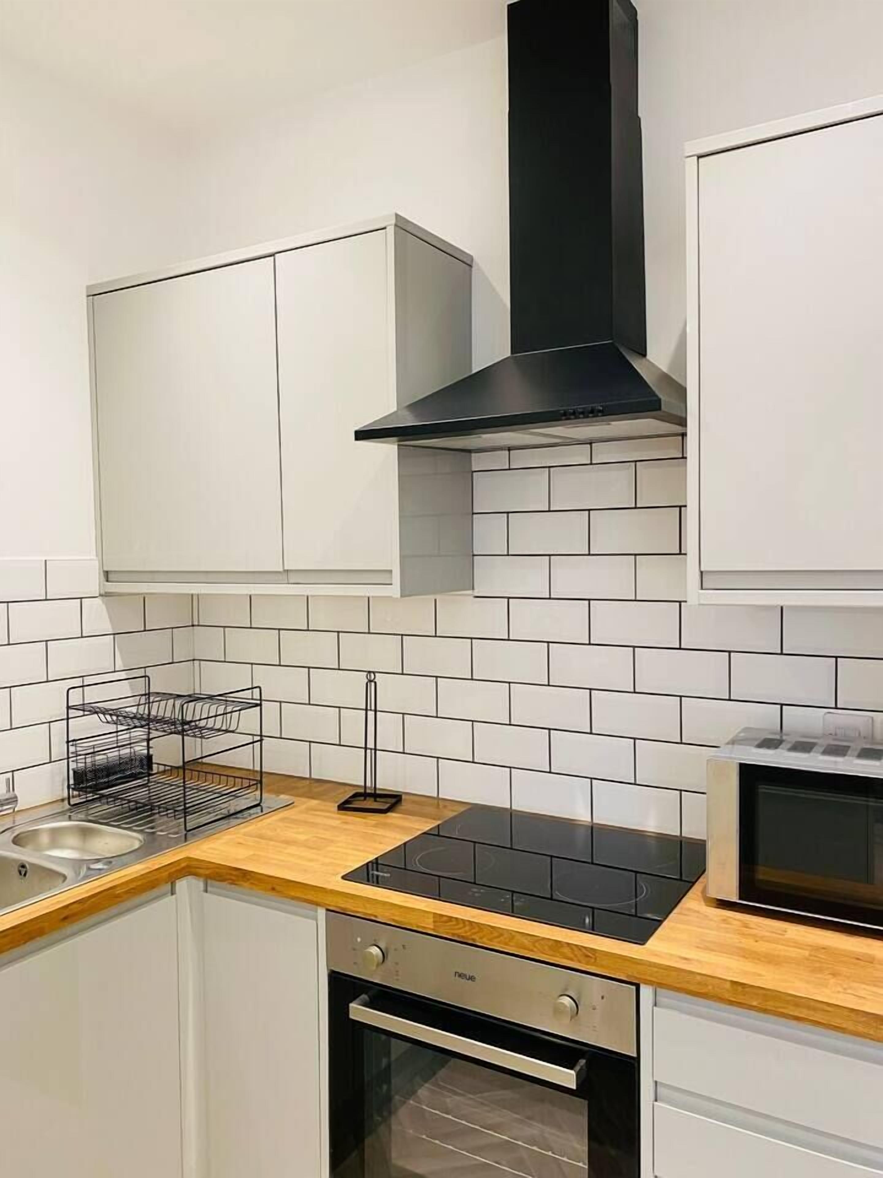 A kitchen with white cabinets, a black range hood, a microwave, and a dishwasher.
