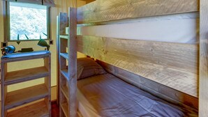 Ein Stockbett mit einer Leiter, ein Schreibtisch mit einer Lampe und ein Fenster mit Blick auf Bäume.