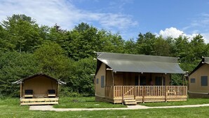 Zwei Holzblockhütten mit Veranda und überdachtem Bereich, umgeben von einer Wiese und dichtem Baumbestand.