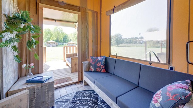 Ein Zimmer mit Holzboden, einer Couch mit floralen Kissen, einem kleinen Tisch mit einer Vase und Blick auf eine Terrasse und Außenbereich.