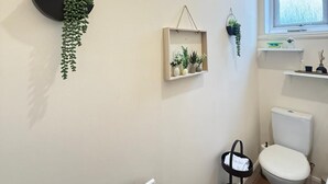 Ein Badezimmer mit Toilette, Heizkörper, Fenster und Wandregalen mit Pflanzen.