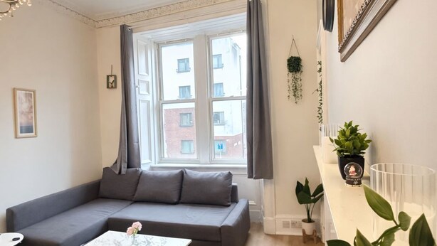 Ein modernes Wohnzimmer mit grauem Sofa, einem Couchtisch und einem großen Fenster mit Vorhängen.