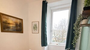 Ein ordentlich gemachtes Bett mit einer karierten Decke, einer Nachttischlampe und einem Fenster mit Vorhängen.