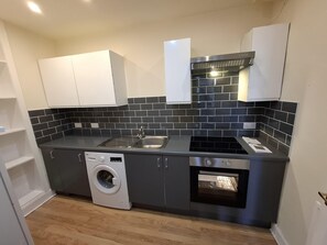 A compact kitchen with a washing machine, a built-in oven, and a sink. - 2BHK Easter Road, Edinburgh (Edinburgh)