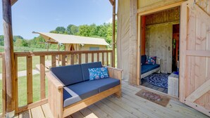 En træterrasse med en sofa og en bænk, et overdækket område og udsigt til et naturområde.