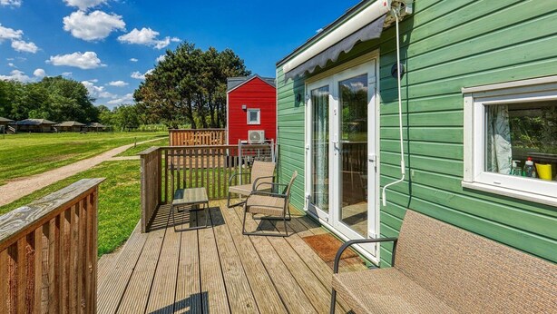 Un bâtiment vert doté d’une terrasse, un bâtiment rouge en arrière-plan et un ciel dégagé.