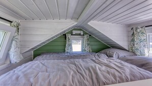 Une chambre avec un plafond en pente, un lit avec une literie grise et une fenêtre avec un rideau.