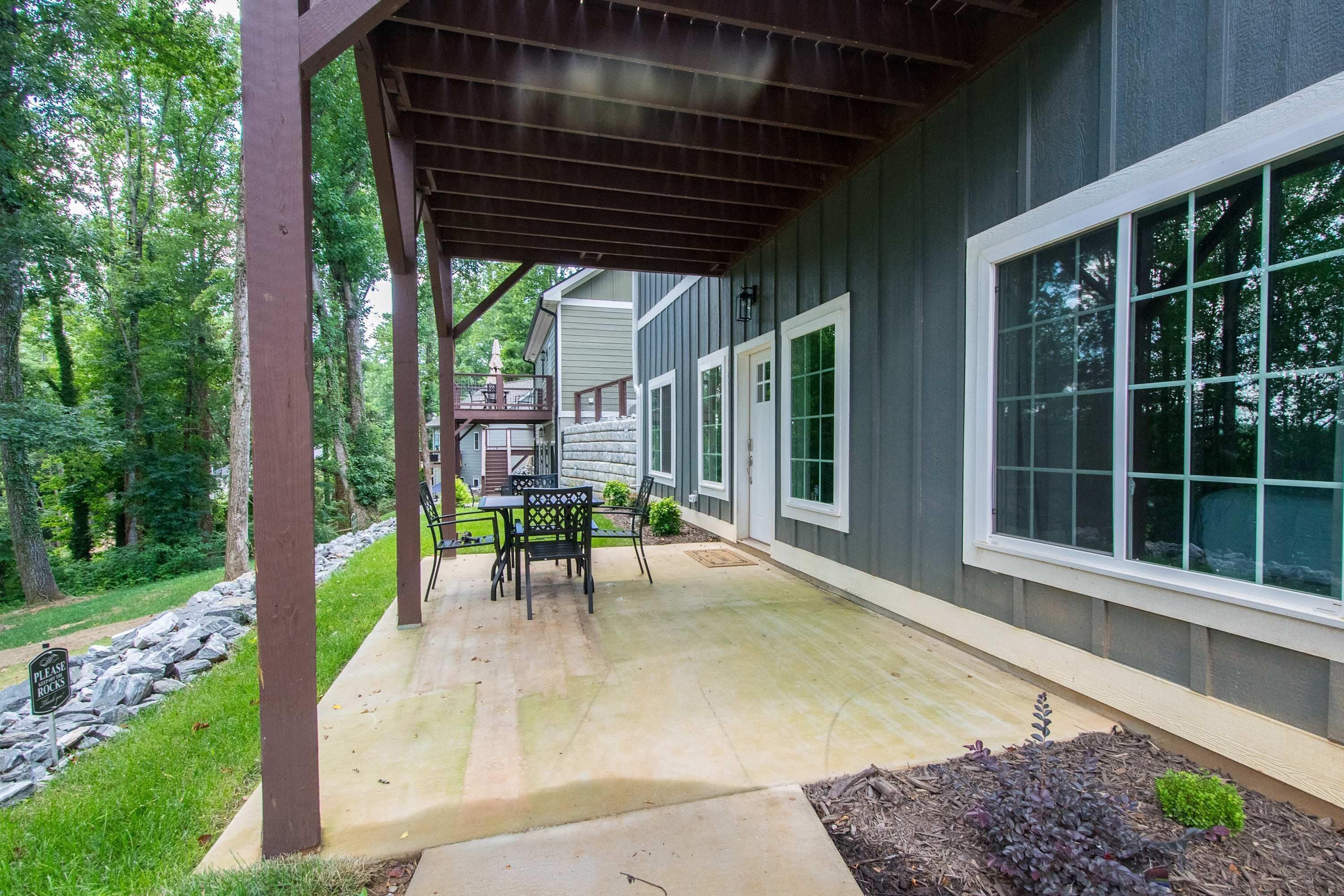 A covered patio area with a table and chairs, a stone wall, and a view of a house with large windows.