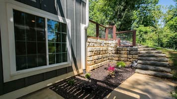 A house with a stone retaining wall, a wooden deck, and a window with a grid pattern.