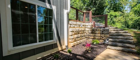 Una casa con un muro de piedra, una terraza de madera y un ventanal con diseño de cuadrícula.