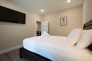 A neatly made bed with white linens in a room with a dark wooden headboard, a flat-screen TV mounted on the wall, and a door leading to another room. - Cozy Lower Retreat II Sleeps 4 Free Tix (Hendersonville)