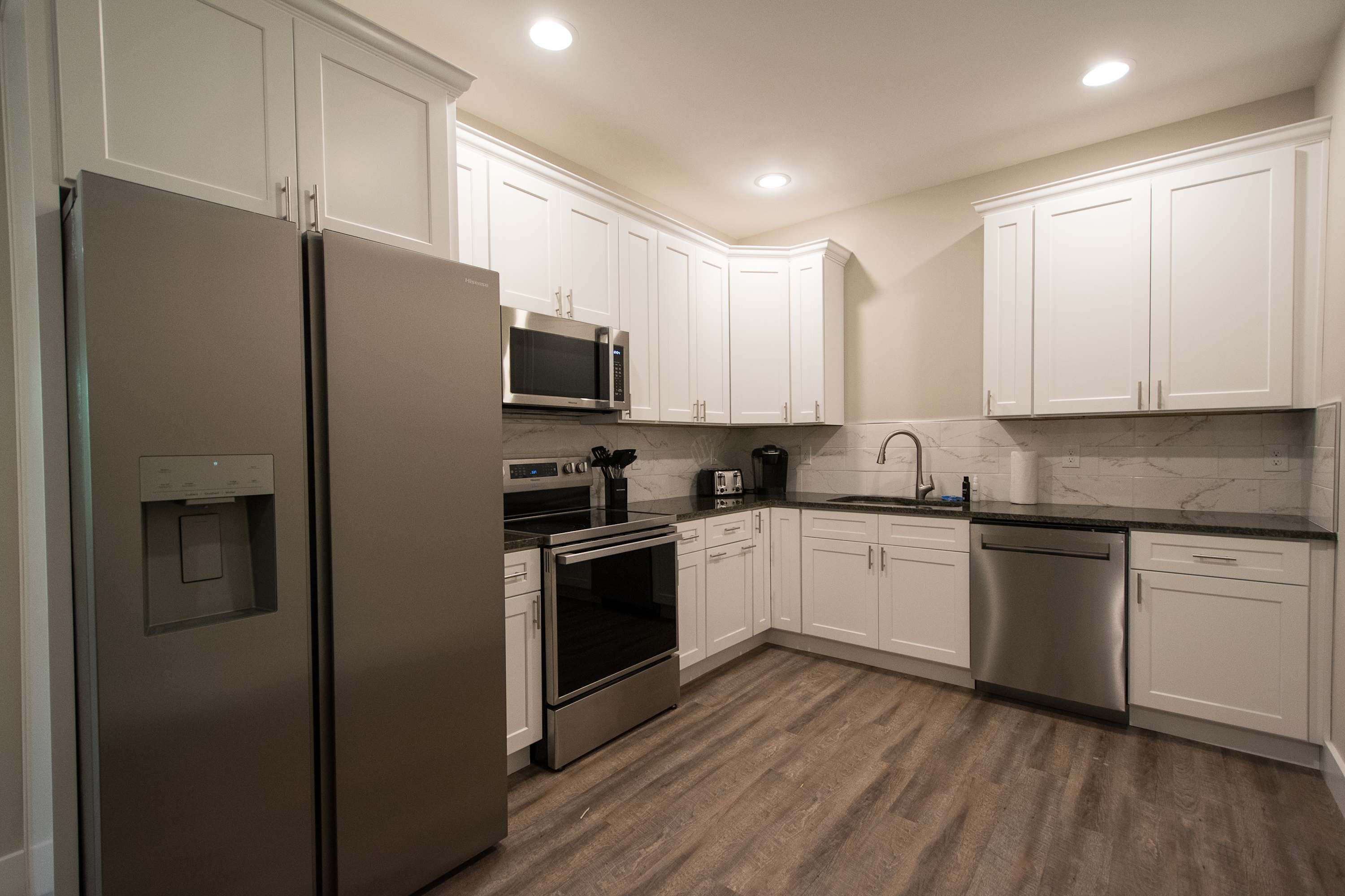 A modern kitchen with white cabinets, stainless steel appliances, and a marble backsplash.