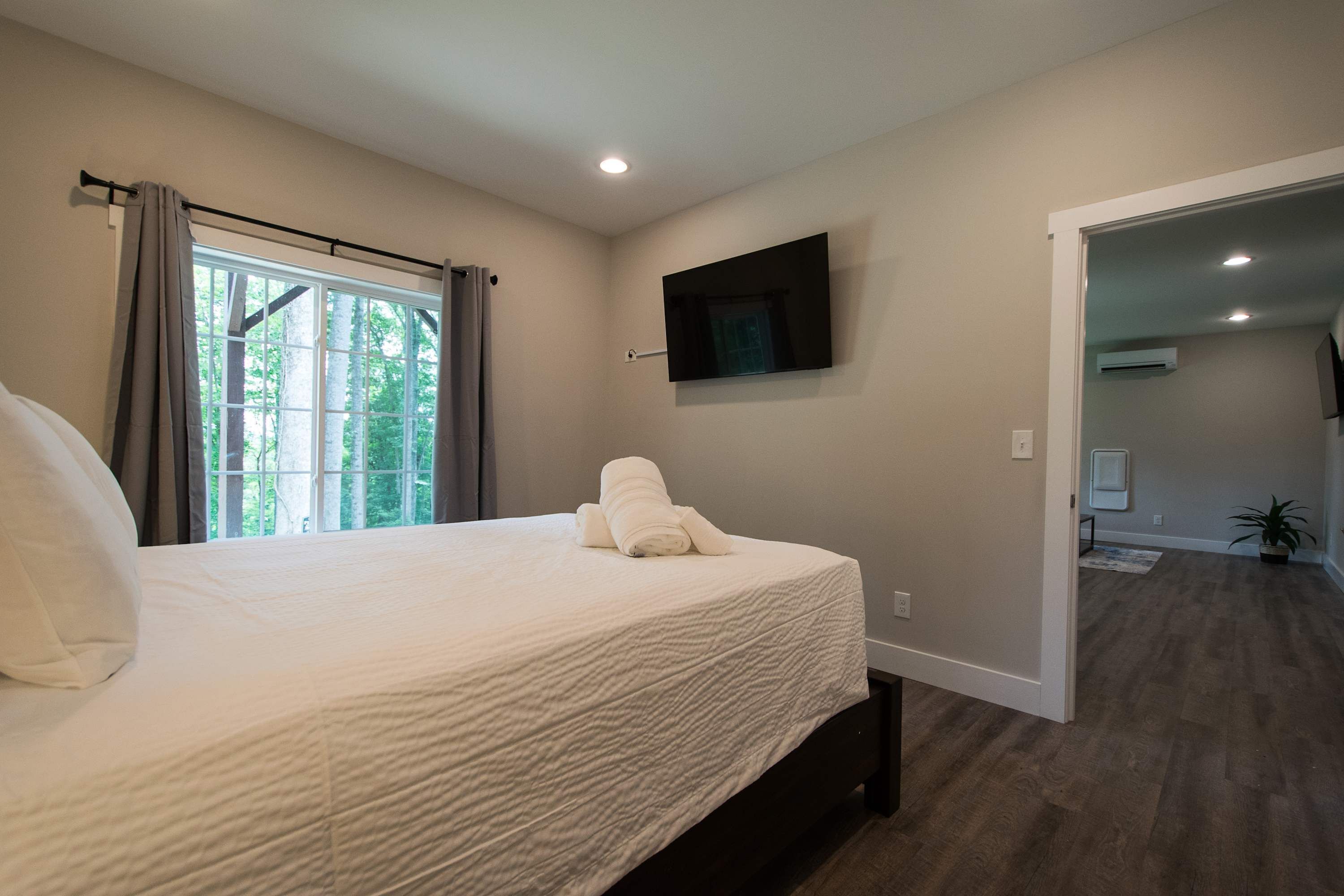 A bedroom with a large bed, a flat-screen TV mounted on the wall, and a window with curtains.