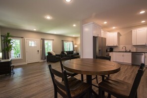 A modern kitchen with white cabinets, a stainless steel refrigerator, and a dining area with a wooden table and chairs. - Cozy Lower Retreat II Sleeps 4 Free Tix (Hendersonville)