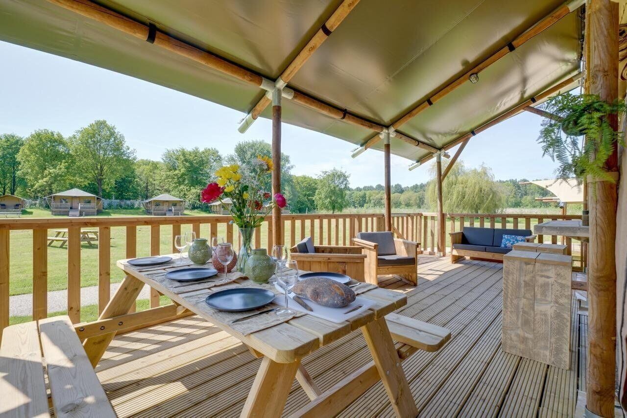 An outdoor wooden deck with a covered seating area, picnic tables, and a view of the surrounding landscape.