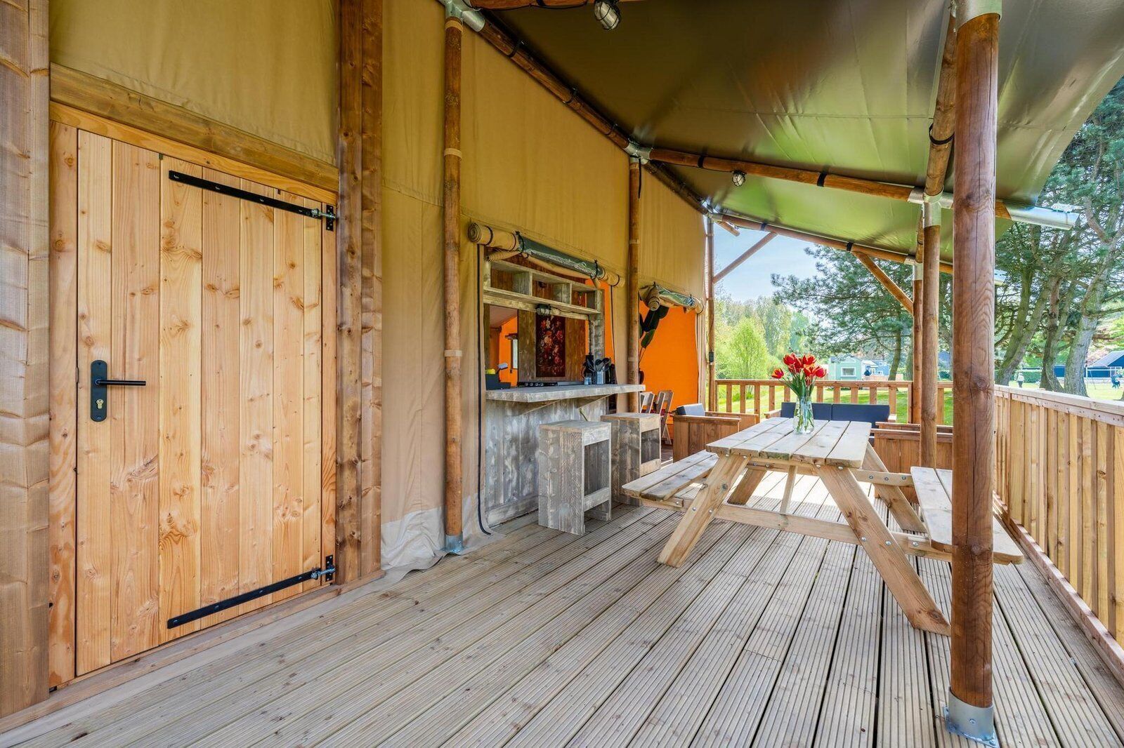 En træterrasse med et overdækket opholdsområde, en bar og udsigt til naturen.