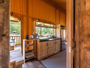 A wooden cabin with a kitchen area, a deck, and a view of the outdoors. - De Glamping - Sunny Trio | 14p (Zeewolde)