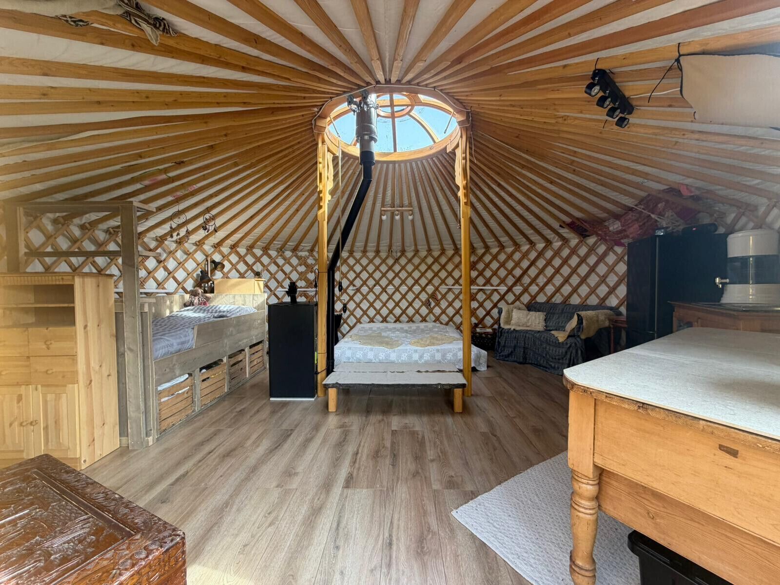 A yurt interior with a central bed, wooden flooring, and a lattice wall.