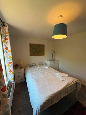A single bed with a white duvet, a bedside table with a lamp, a small bedside plant, and a wall-mounted artwork. - #170 Modern 2BR Coventry Stay - Sleeps 4 (West Midlands)