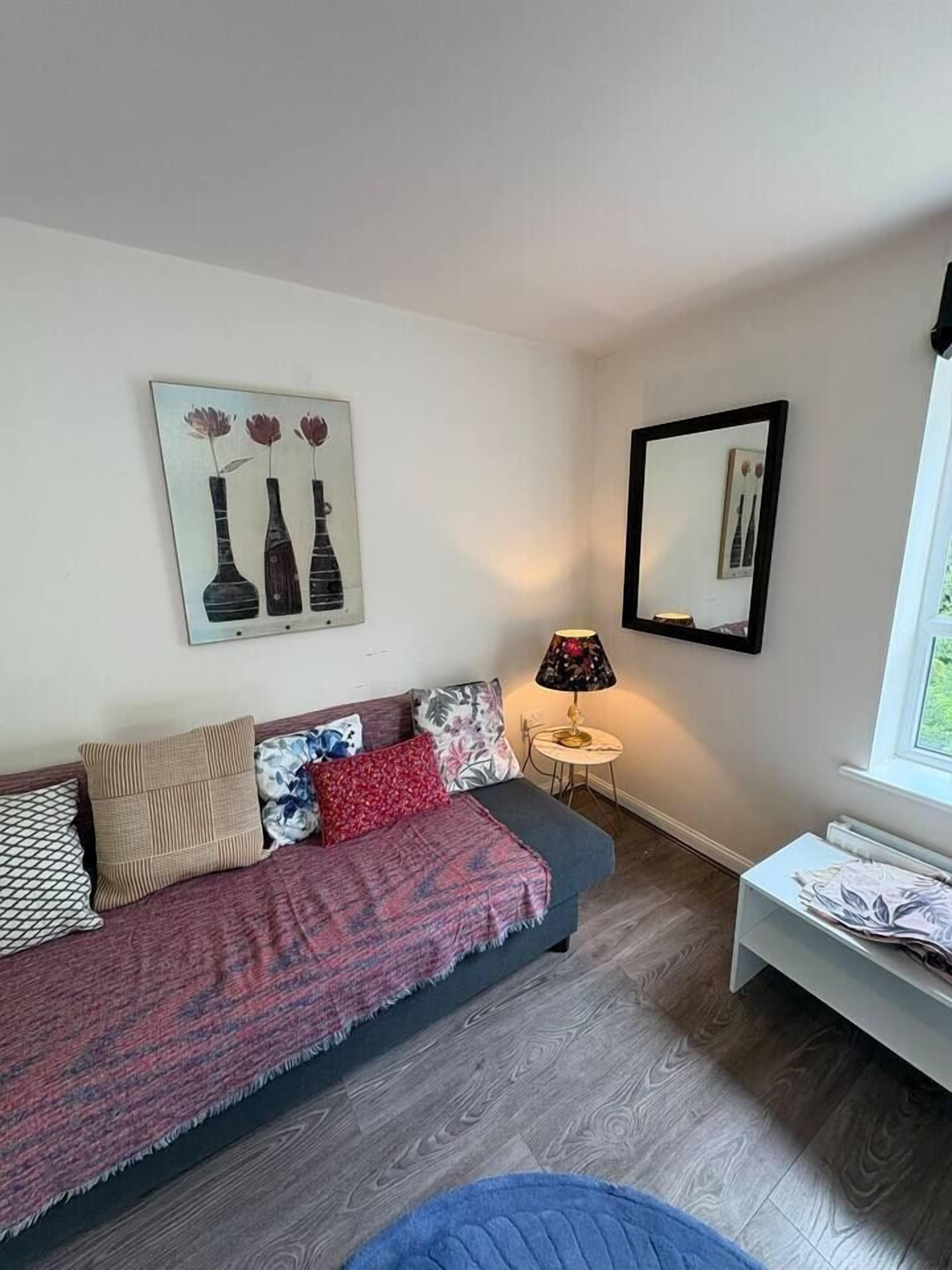 Une chambre meublée avec un canapé, une petite table, une lampe et une fenêtre.