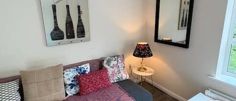A furnished room with a sofa, a small table, a lamp, and a window.