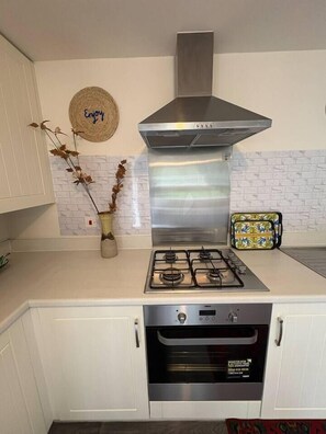 A kitchen with a gas stove, oven, stainless steel range hood, white cabinets, and a decorative wall piece. - #170 Modern 2BR Coventry Stay - Sleeps 4 (West Midlands)