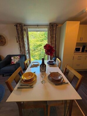 A dining area with a table set for four, a vase with flowers, and a view of greenery outside. - #170 Modern 2BR Coventry Stay - Sleeps 4 (West Midlands)