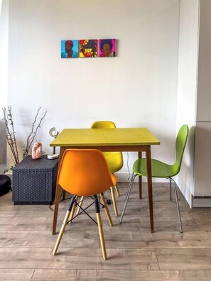A dining area with a yellow table, orange and green chairs, and a wall-mounted artwork. - #177 Stylish Finsbury Park Retreat - Sleeps 2 (Greater London)