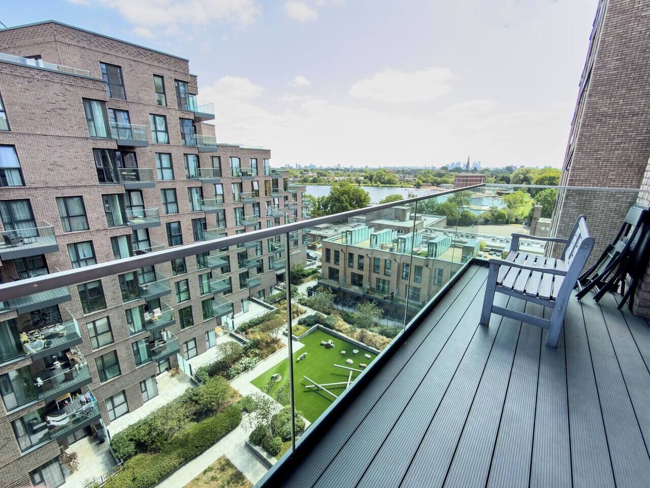 A high-rise building with multiple balconies, a rooftop garden, and a view of a river and cityscape.
