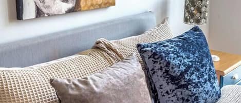 Un dormitorio con cama, almohadas, un cuadro en la pared y una mesita de noche con lámpara.