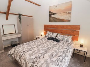 A bedroom with a bed, a nightstand, a bedside lamp, a wardrobe, a mirror, and a painting of a beach scene. - 41 St James Street (Narberth)