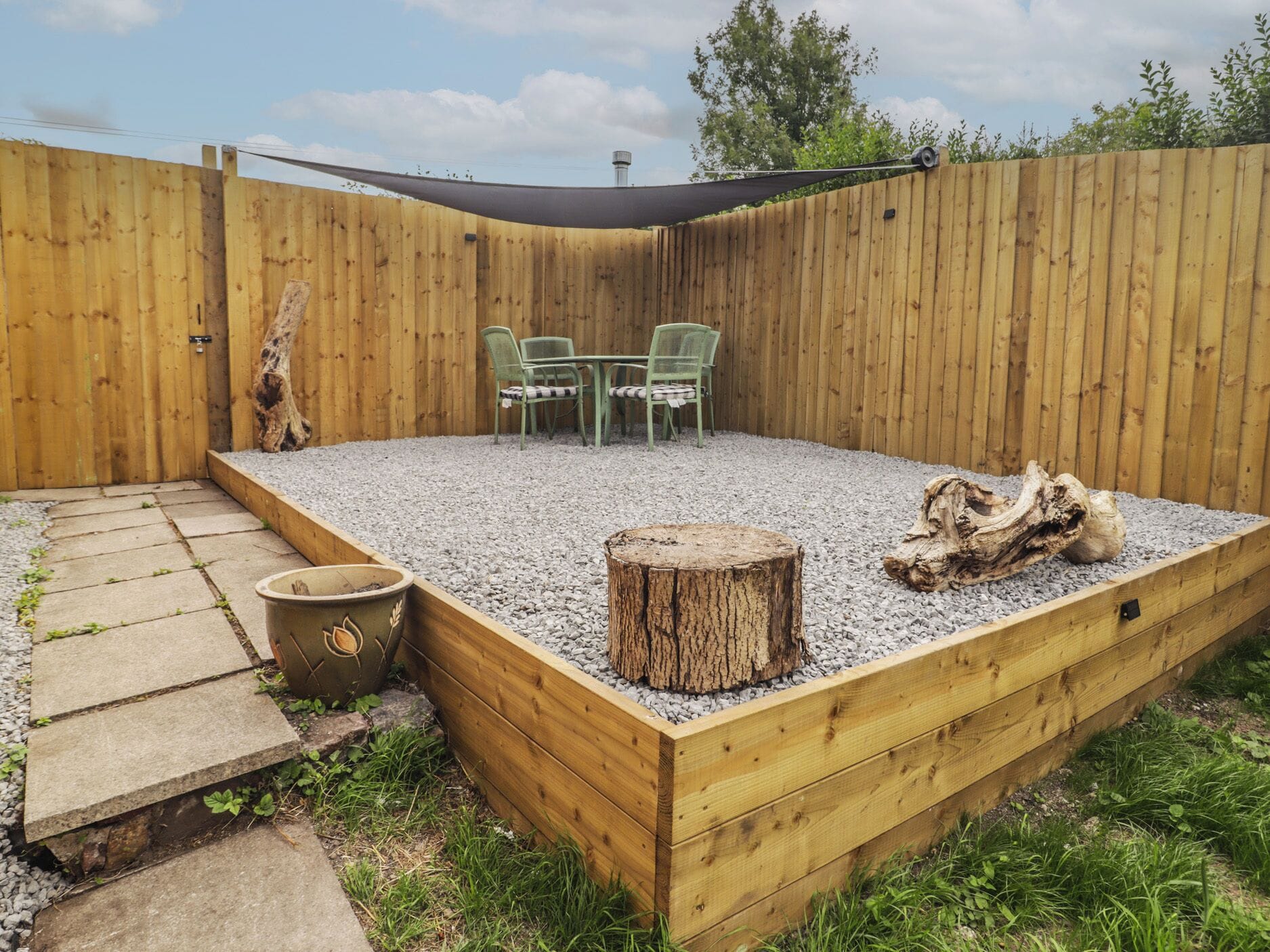 A wooden deck with a table and chairs, surrounded by a wooden fence and a shaded area.