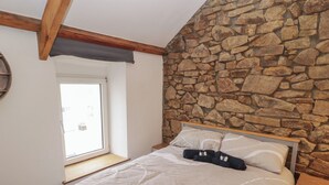 Ein Schlafzimmer mit Stehwand, einem Bett mit weißer Bettwäsche, einem hölzernen Kopfteil und einem Fenster mit Blick.