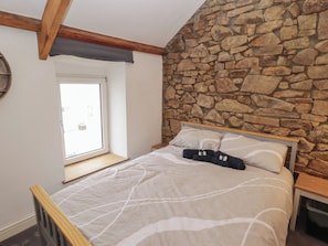 A bedroom with a stone wall, a bed with white bedding, a wooden headboard, and a window with a view. - 41 St. James Street (Narberth)