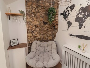 A cozy room with a stone wall, a grey cushioned chair, a world map, and a shelf with a bottle and glasses. - 41 St. James Street (Narberth)