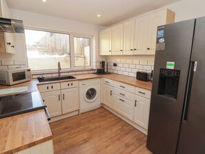 A modern kitchen with white cabinets, a stainless steel refrigerator, a washing machine, and a microwave. - 41 St James Street (Narberth)